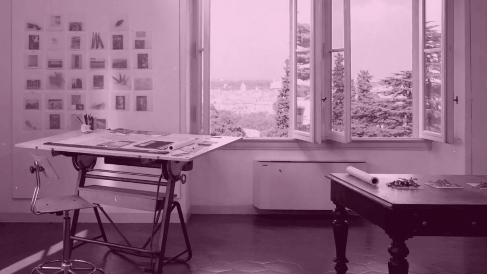 Photograph of an artist's studio showing a work desk, stool, wooden table, and open windows