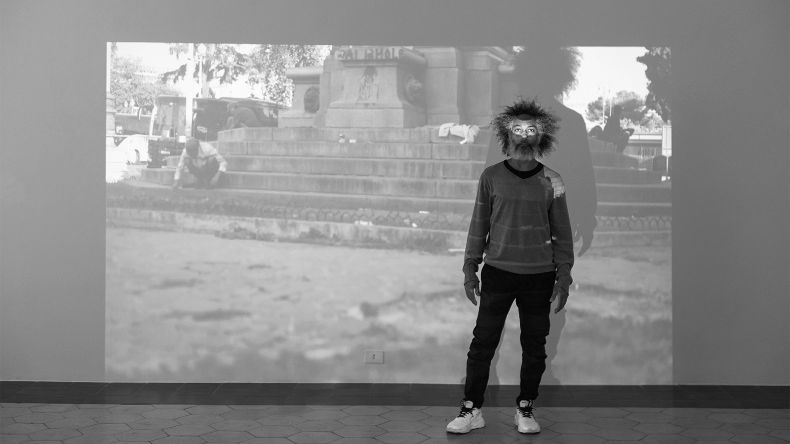 black and white photo of an african american man standing in front of a wall-sized projection of his art video