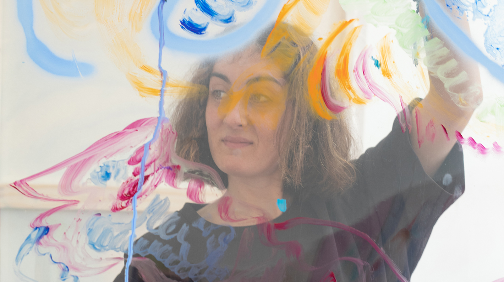 Color photograph of the head and shoulders of a light skinned woman with brown hair; she holds a translucent sheet in front of her that is covered with colorful swirls