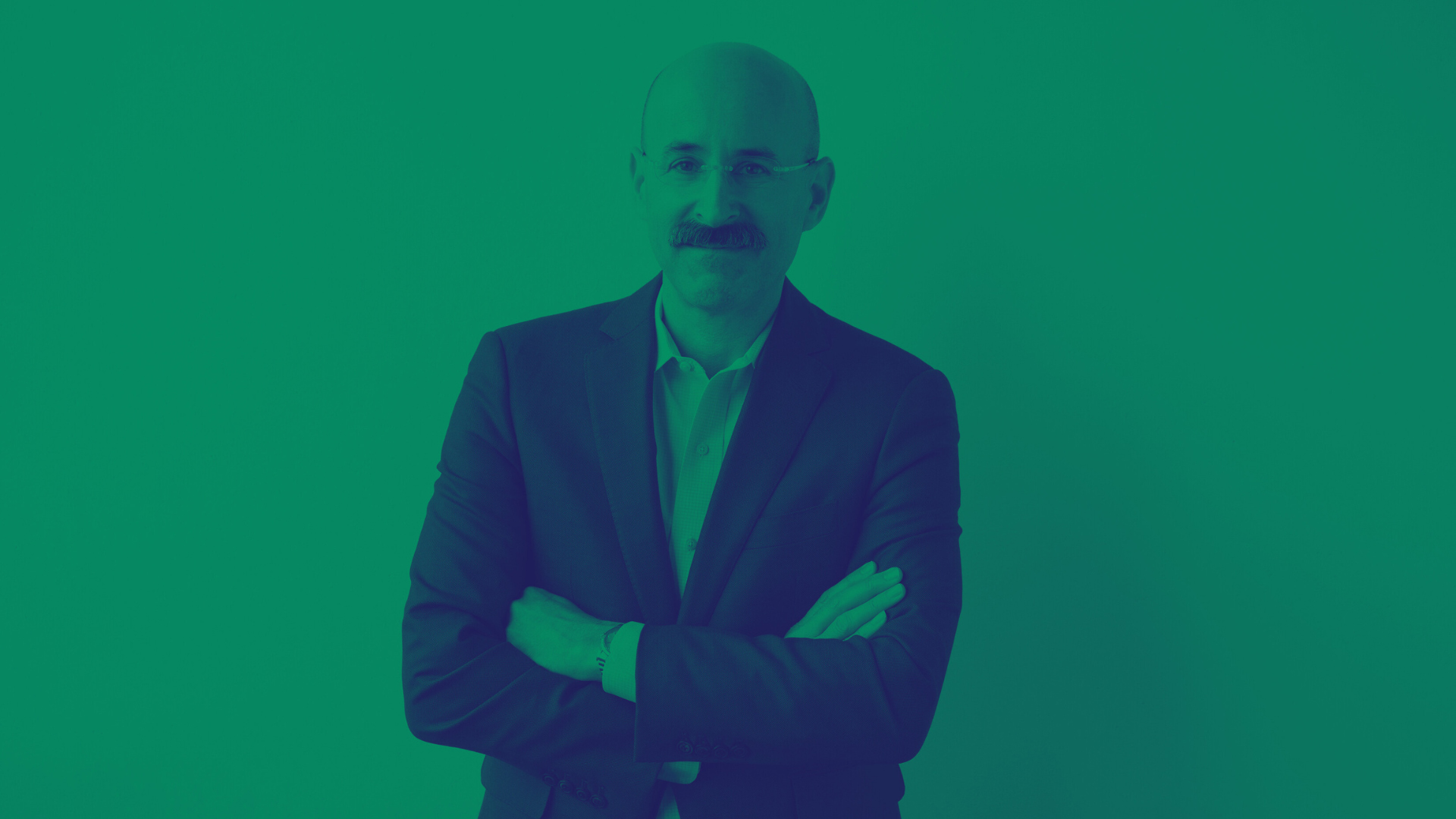 Adam Yarinsky Photograph of a light skinned man wearing a dark suit with his arms folded; he wears glasses and a mustache and smiles at the camera