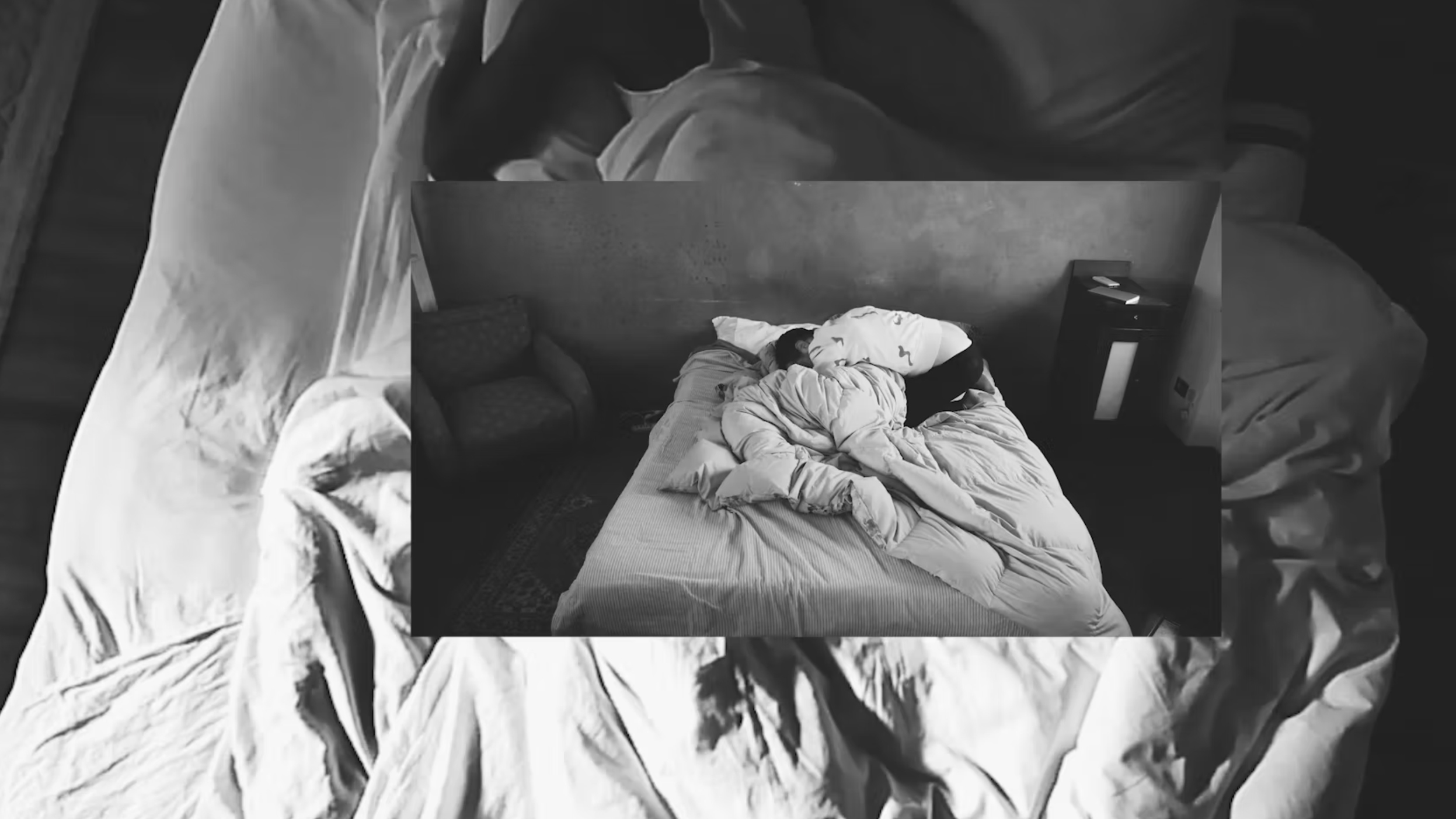 LETTO Autumn Knight Black and white photograph of a man crouched face down on a bed with blankets and pillows, placed on top of an enlarged version of that same image