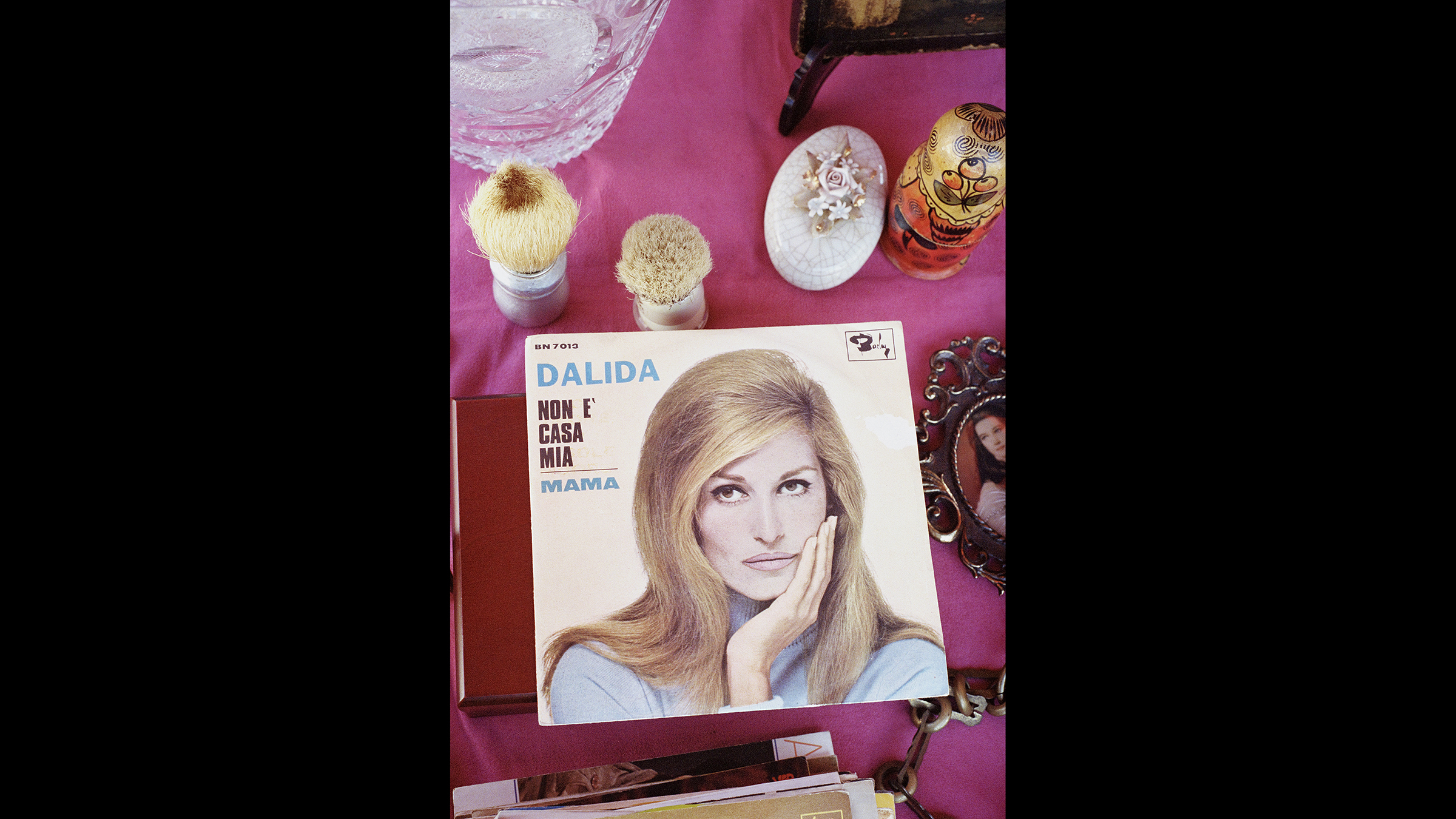 Liana Miuccio black Color photograph of a tabletop with a pink cloth cover; on top is a record cover with a light skinned woman's face and assorted brushes