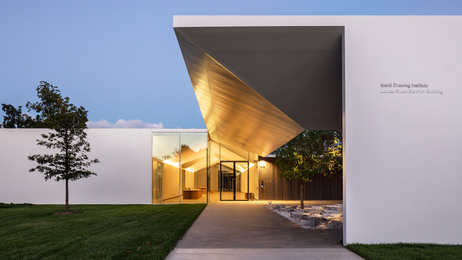 Mark Lee Discorso Color photograph of a twenty-first century museum building at dusk or dawn, taken at ground level looking straight toward the boxy square light colored stone structure