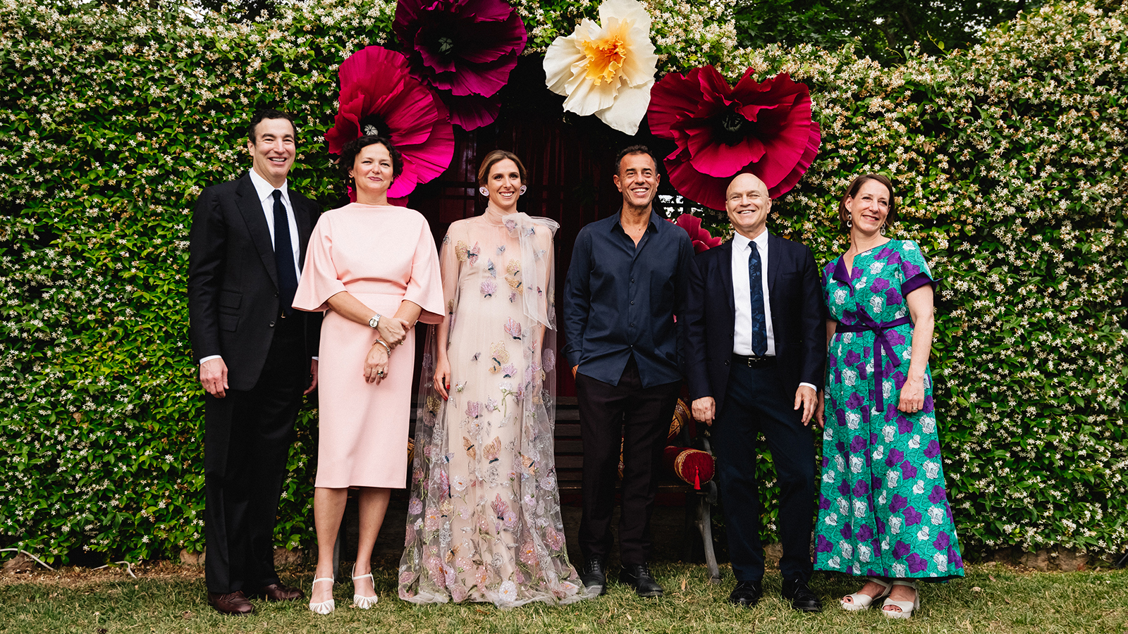 McKim Medal Gala 2022 Honorees A group of six men and women wearing gala attire and posting in front of a green hedge with large artificial flowers above them