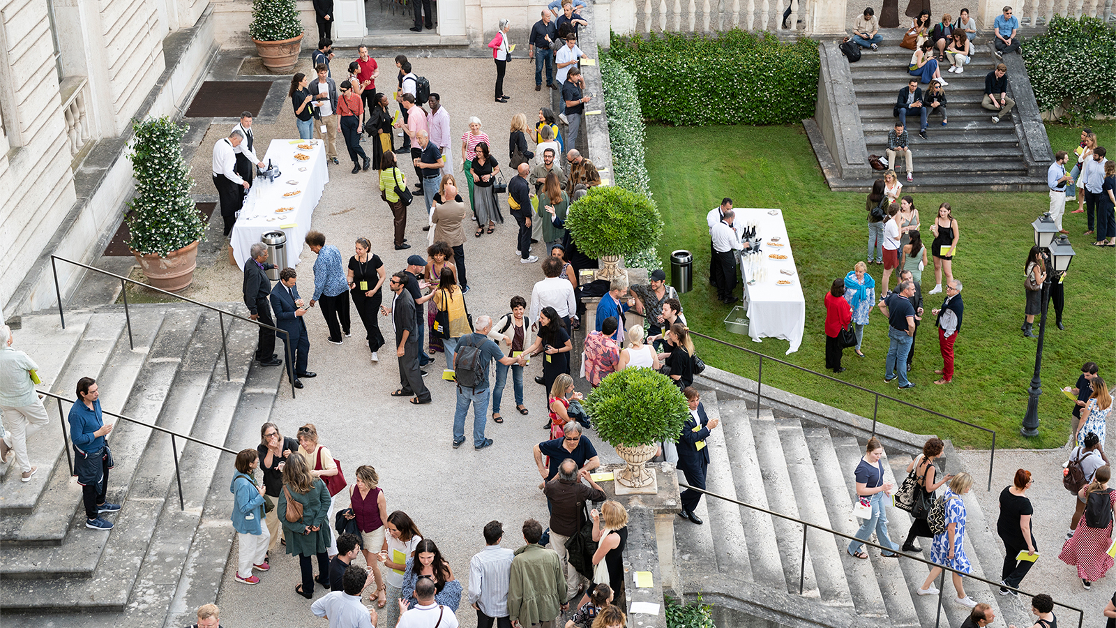 Open Studios 2024 Color photo of an outdoor gathering of several dozen people on the front steps of a large building in Rome that has a grass lawn