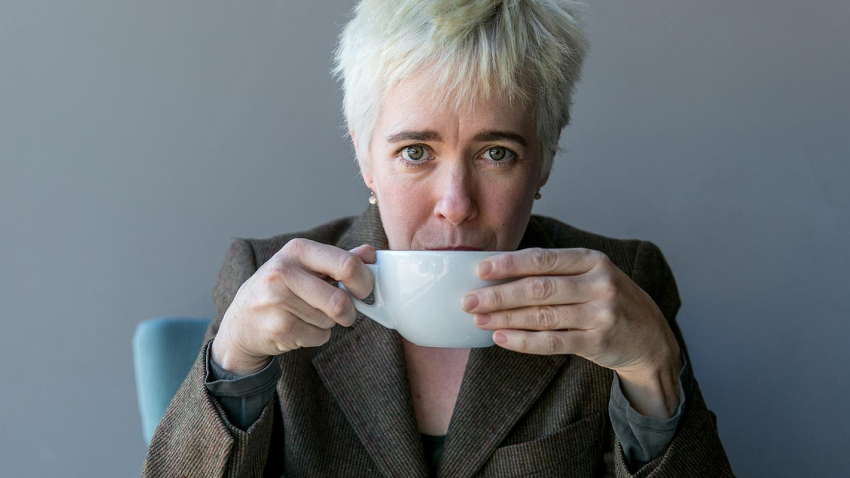 Color photograph of Kate Thomas drinking a beverage from a large white ceramic mug