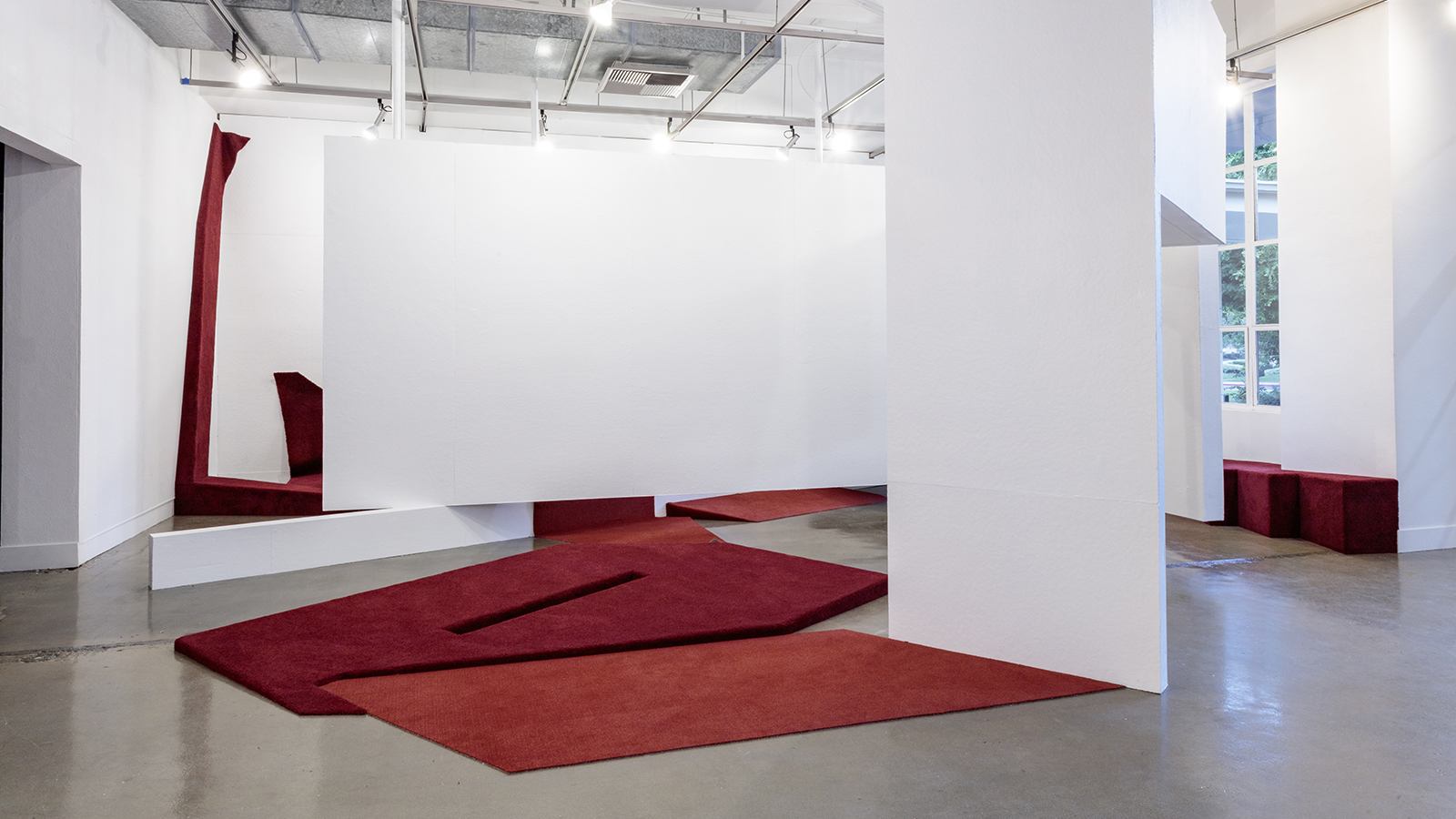 Shoptalk - Katy Barkan Color photographs of an architectural installation of temporary white walls and low, angled red-carpet-covered platforms and ramps