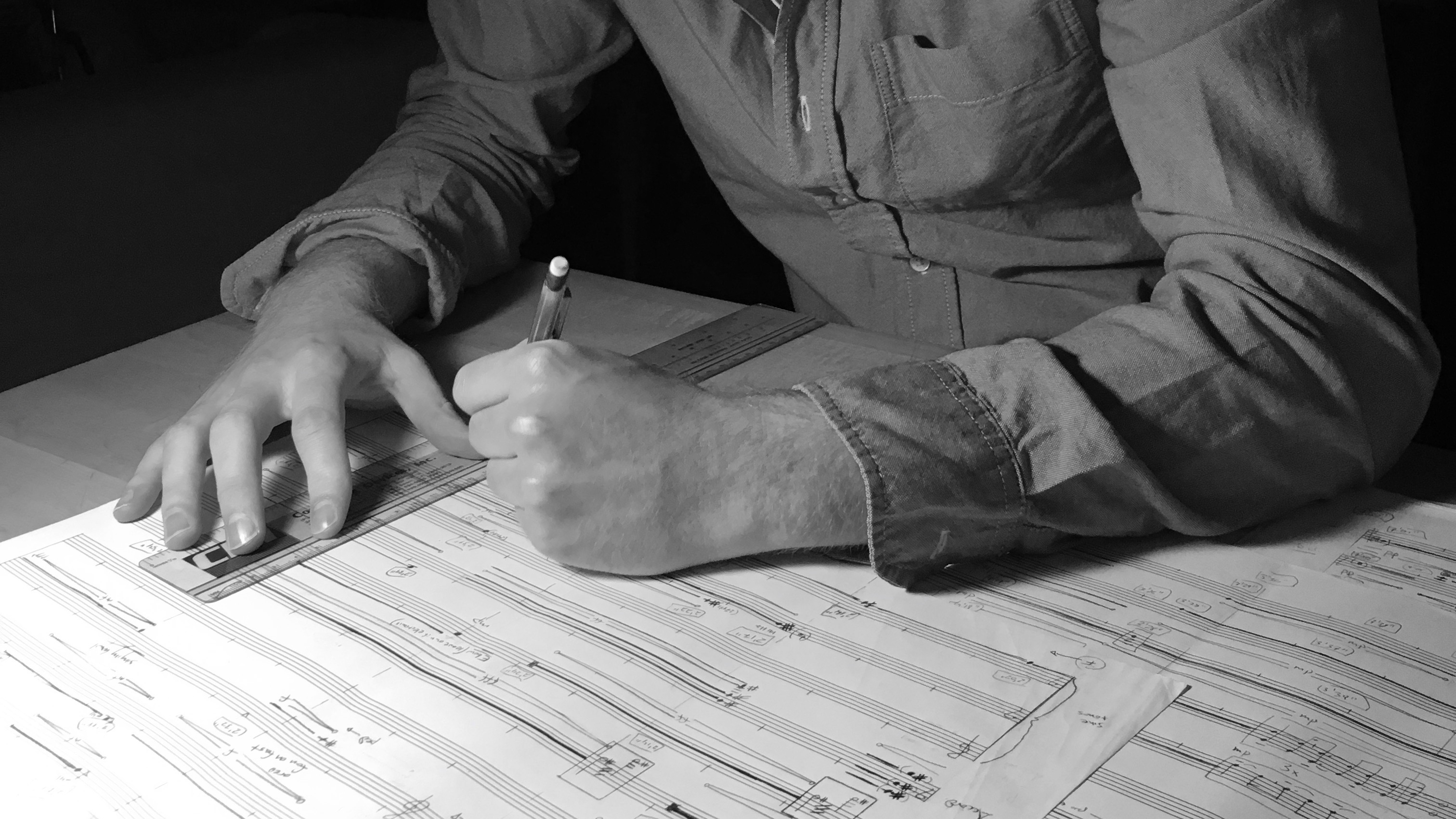 Shoptalk - William Dougherty Black and white photograph of William Dougherty's arms and hands as he writes notation on a musical score sheet