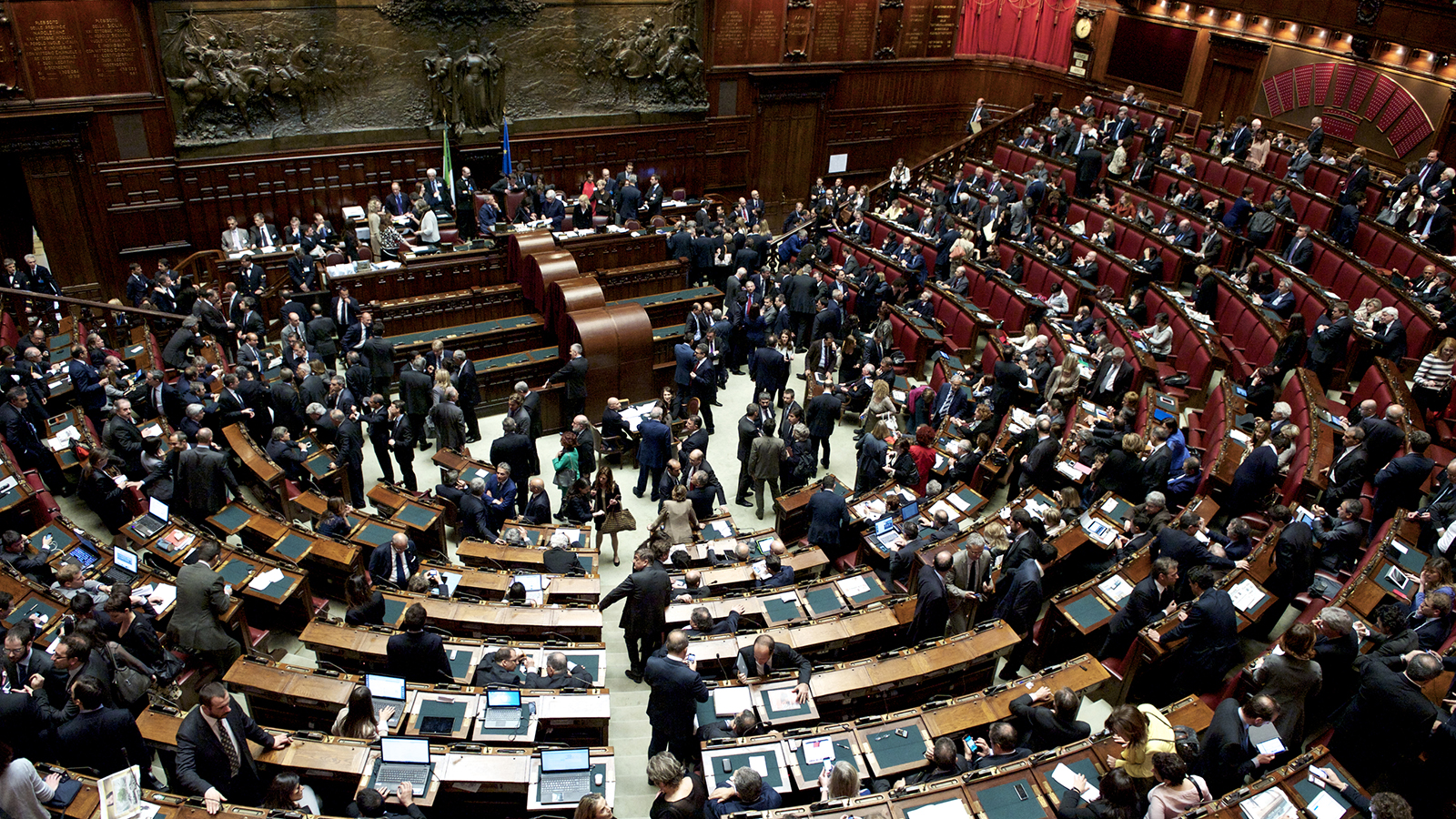 What Next for Italian Politics Balcony view of the interior of Italian parliament with politicians milling about a semicircle of desks and chairs