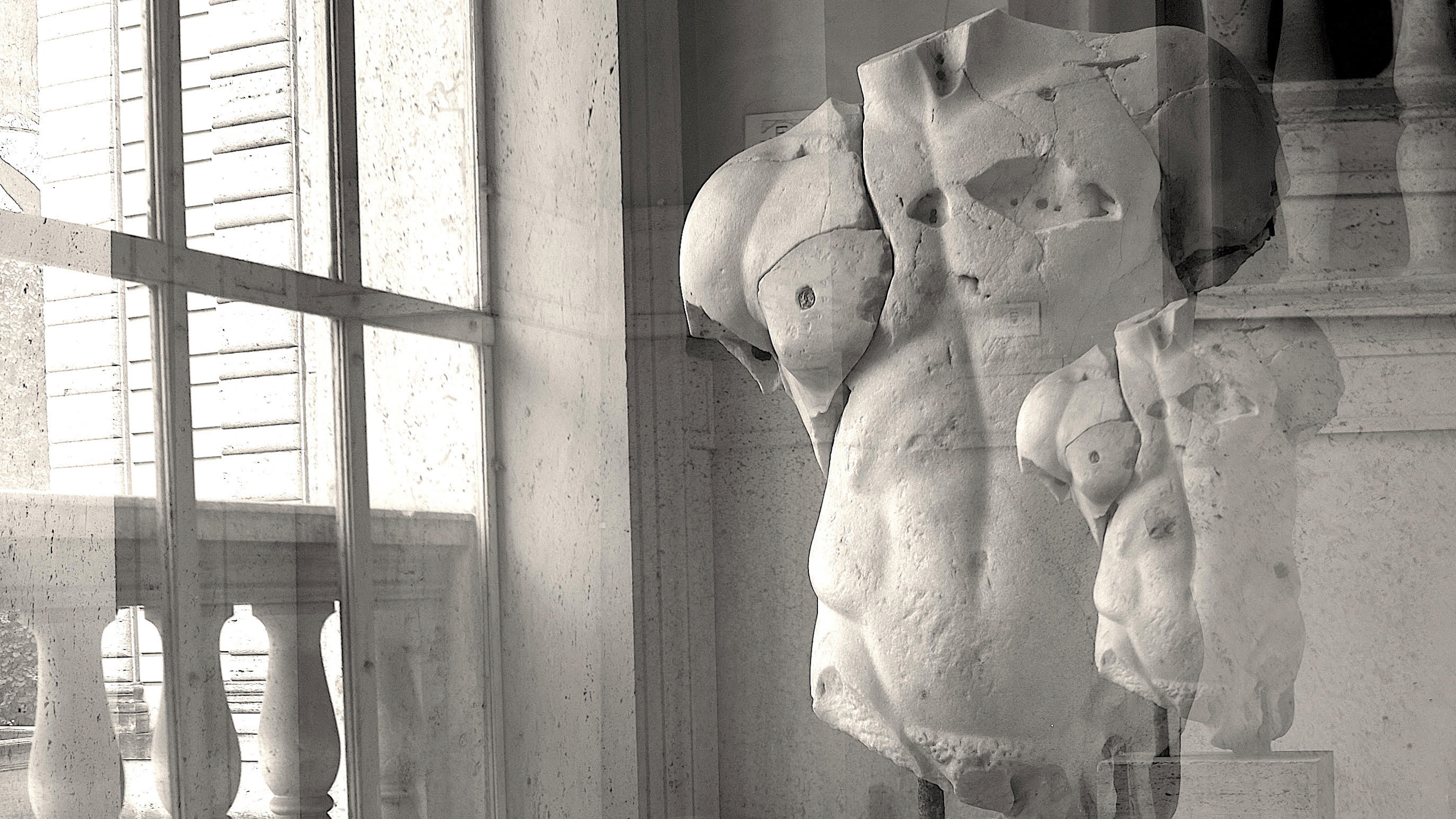 Winter Open Studios 2023 Black and white photograph of the torso of an ancient Roman sculpture (without a head, legs, and arms) next to a paned glass window