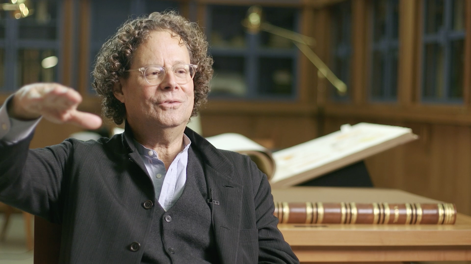 Color video still of a light skinned man being interviewed on camera in a rare book library
