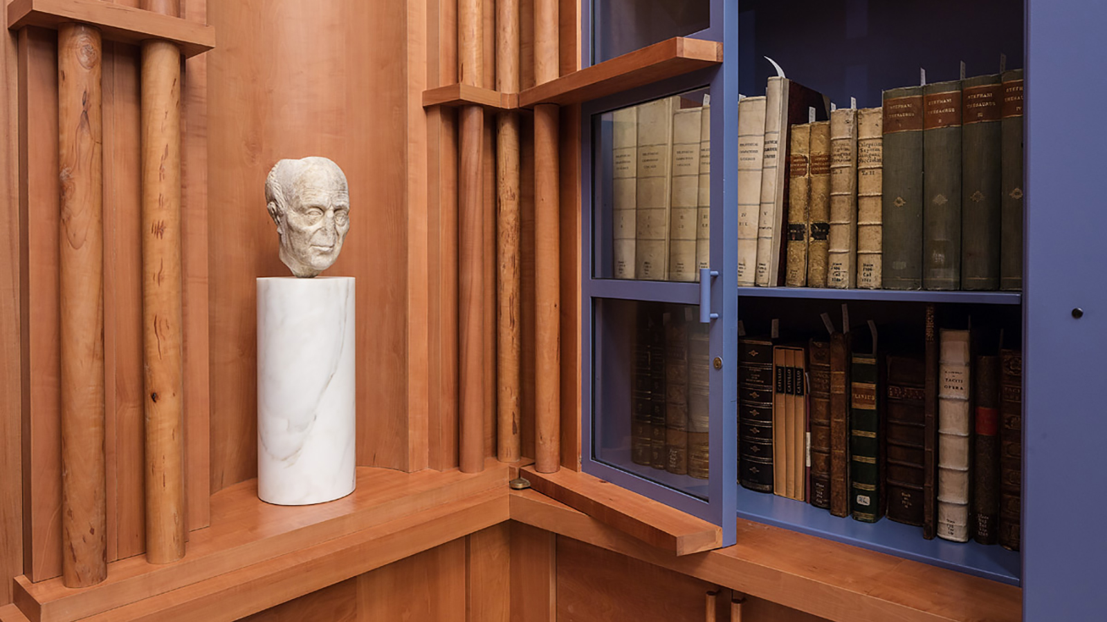 color photograph of a library room with books on shelves to the left and a roman sculpture of a small head on a pedestal on the right