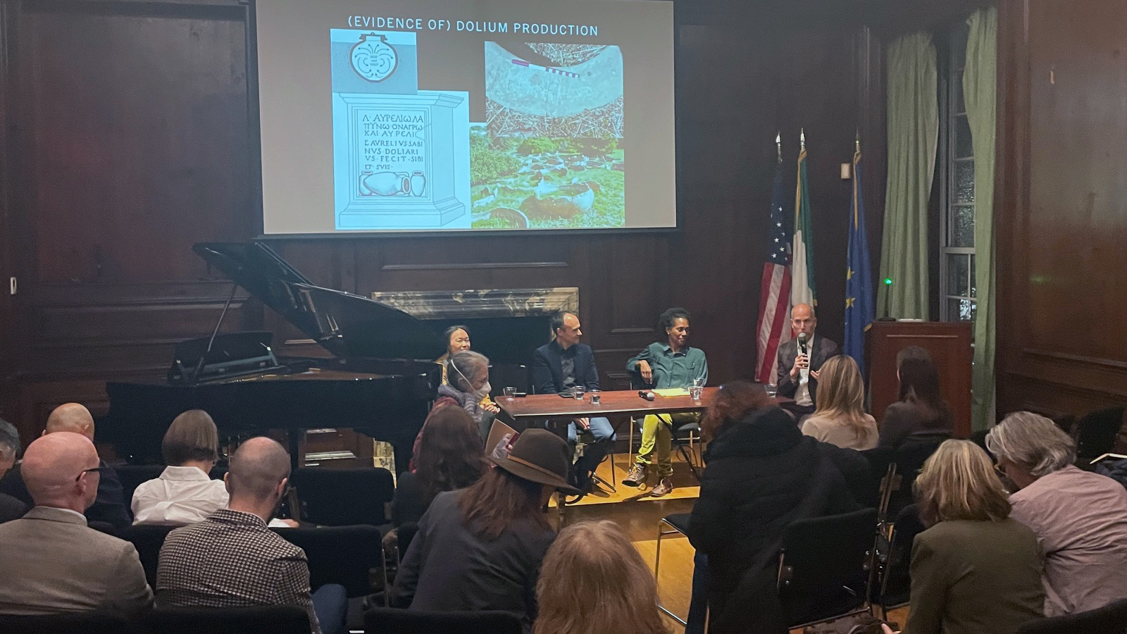 Color photo of a small auditorium with people in chairs and speakers at a table