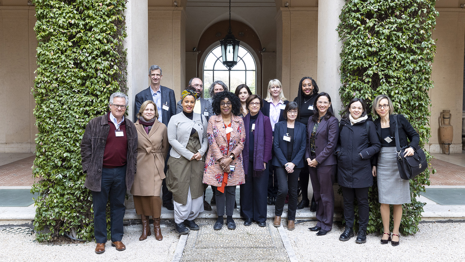 Color photograph of a mix of people standing in two rows in a courtyard; everyone is posed and looking at the camera