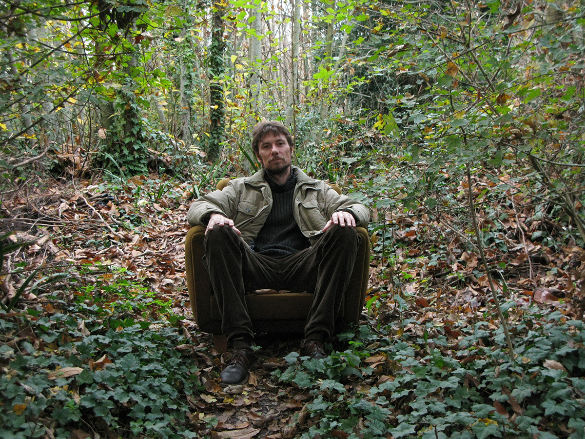 Alessandro Mulazzani Color photograph of a light skinned man with brown hair and beard sitting in an easy chair in the middle of a forest and looking directly at the camera