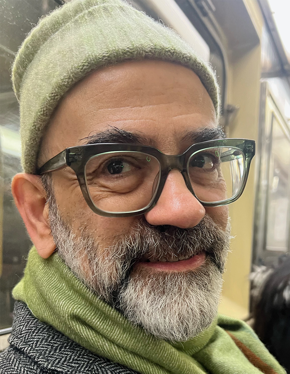 Alexander Nagel Color photo of the head and shoulders of a light skinned man smiling at the camera; he wears glasses, a cap, and a beard