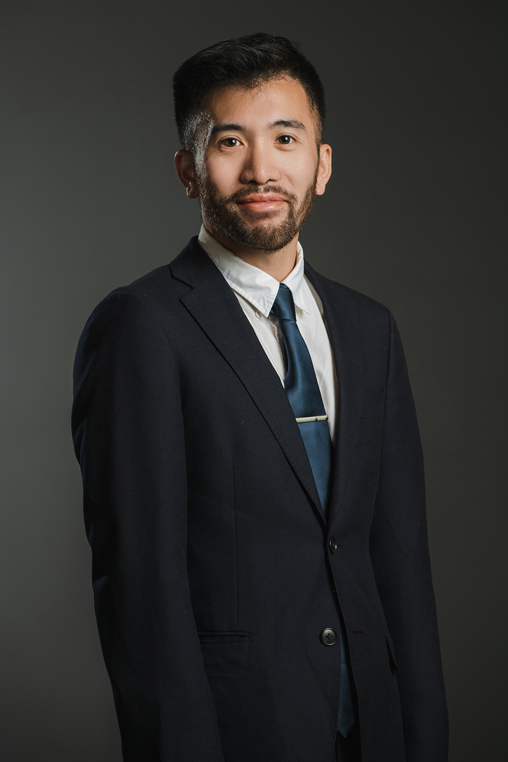 Baldwin Giang Color photograph of an Asian man with dark hair wearing a dark suit and tie as he looks at the camera