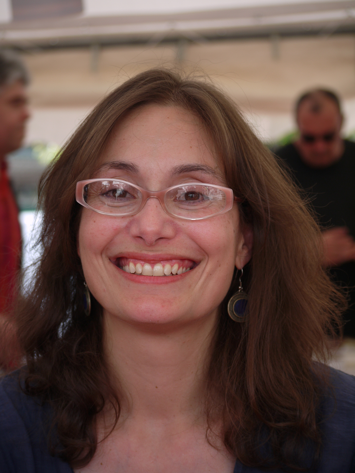 Dana Spiotta Color photograph of the head of a light skinned dark haired woman wearing glasses and smiling broadly at the camera
