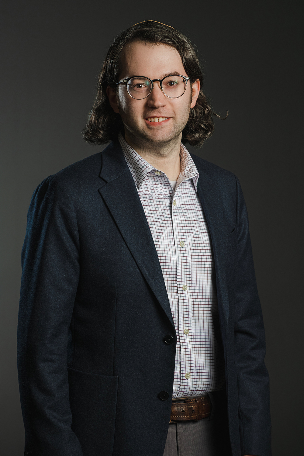 Dov Honick Color photograph of a light skinned man wearing glasses and a dark blazer over a plaid shirt; he looks at the camera confidently