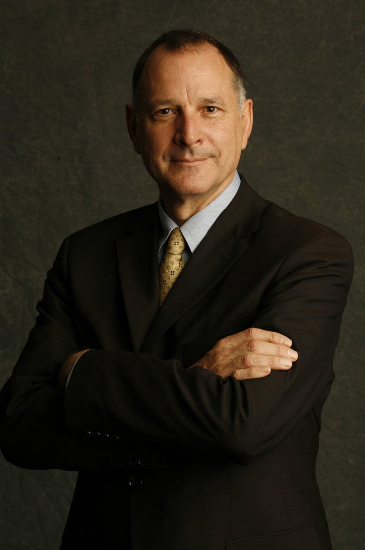 Frederick Fisher Color photograph of the head and torso of a light skinned man wearing a dark suit and tie and smiling slightly at the camera