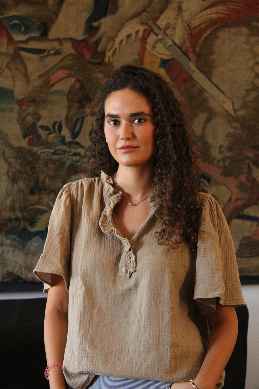 Color photo of a light skinned woman standing in front of a tapestry