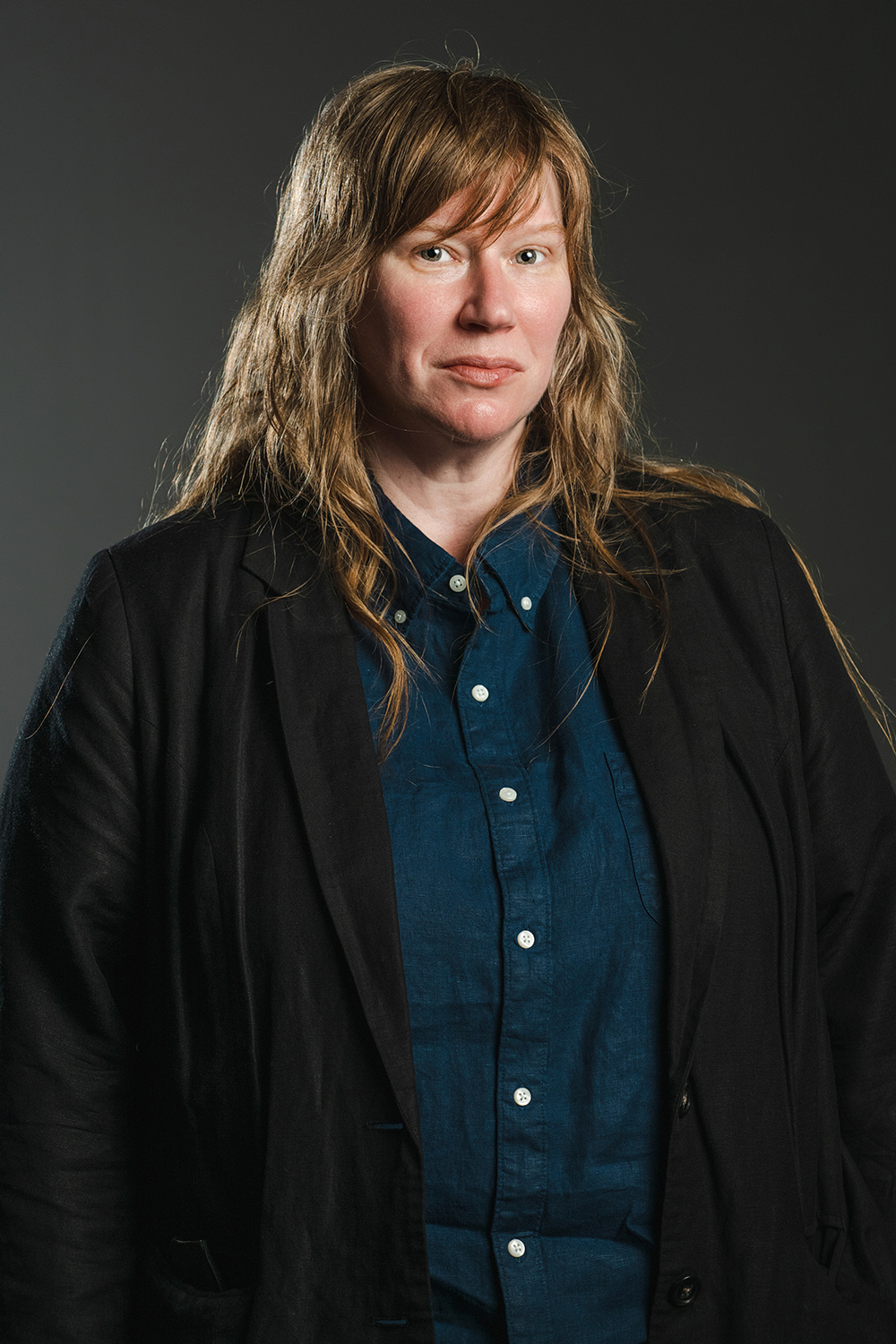 Jeanine Oleson Color photograph of a light skinned woman with brown hair wearing a black blazer over an indigo shirt; she looks at the camera with a serious expression