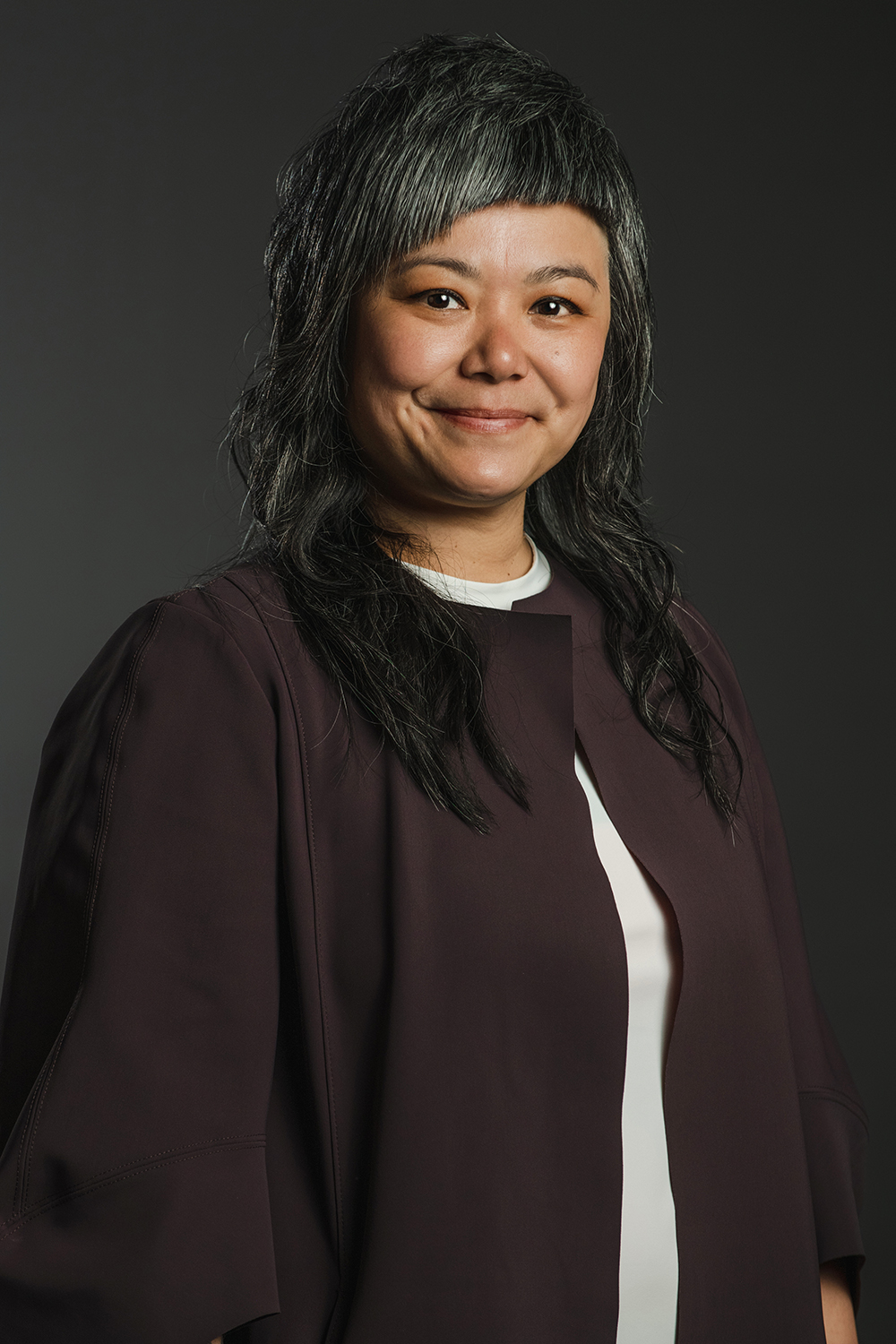 Lan Tuazon Color photograph of an Asian woman with black and gray hair and a black jacket; she smiles at the camera