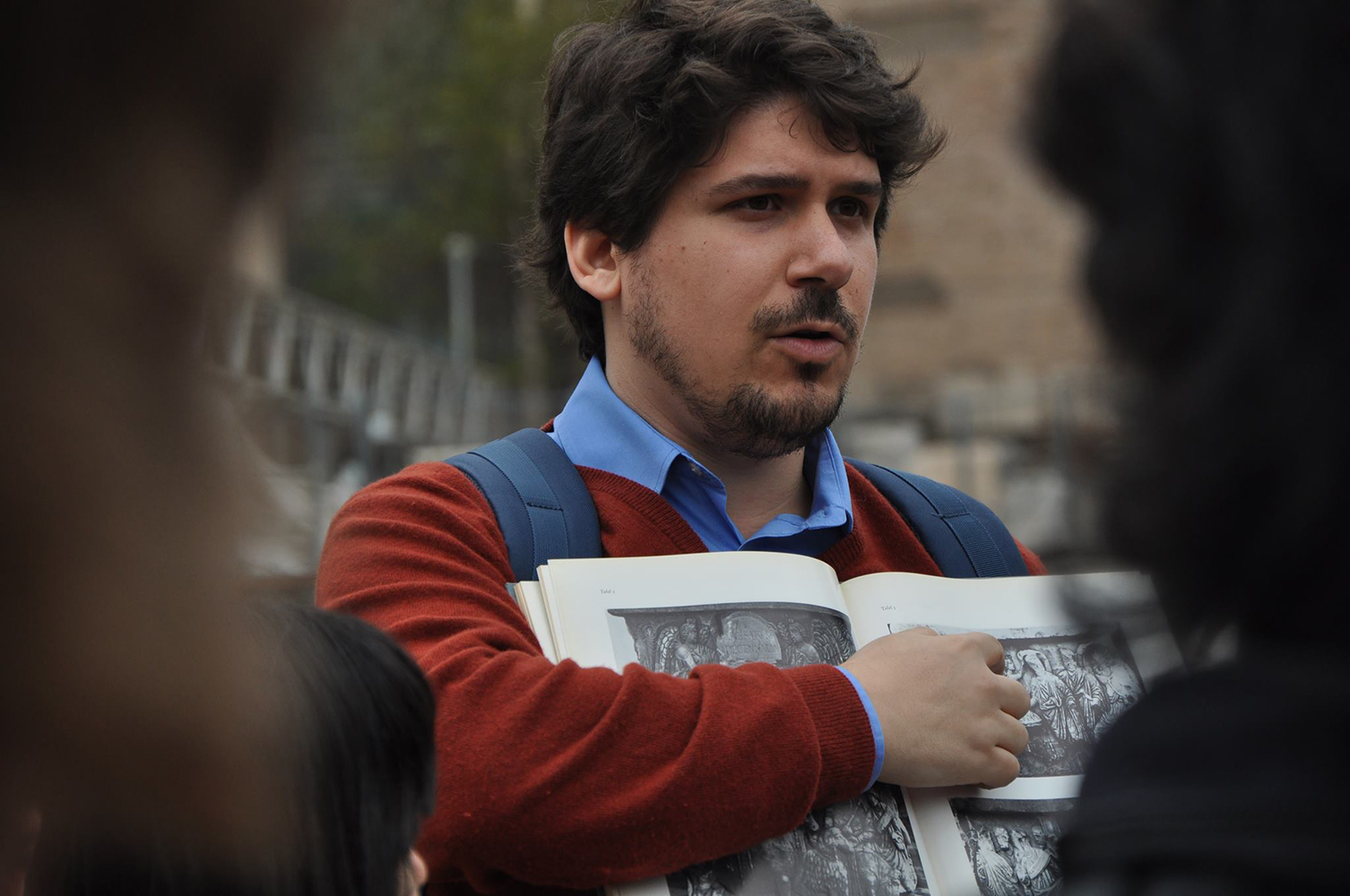 Nicola Barbagli Color photograph of a light skinned man with dark hair holding a book and pointing to something in it