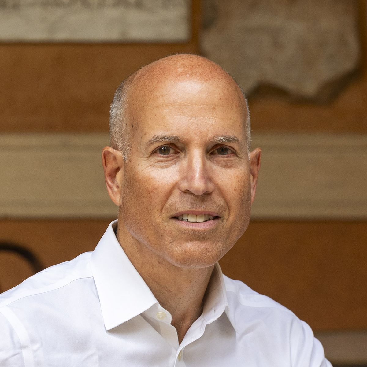 Peter N. Miller Color photograph of a light skinned man wearing a white shirt and sitting at a cafe table, smiling at the camera