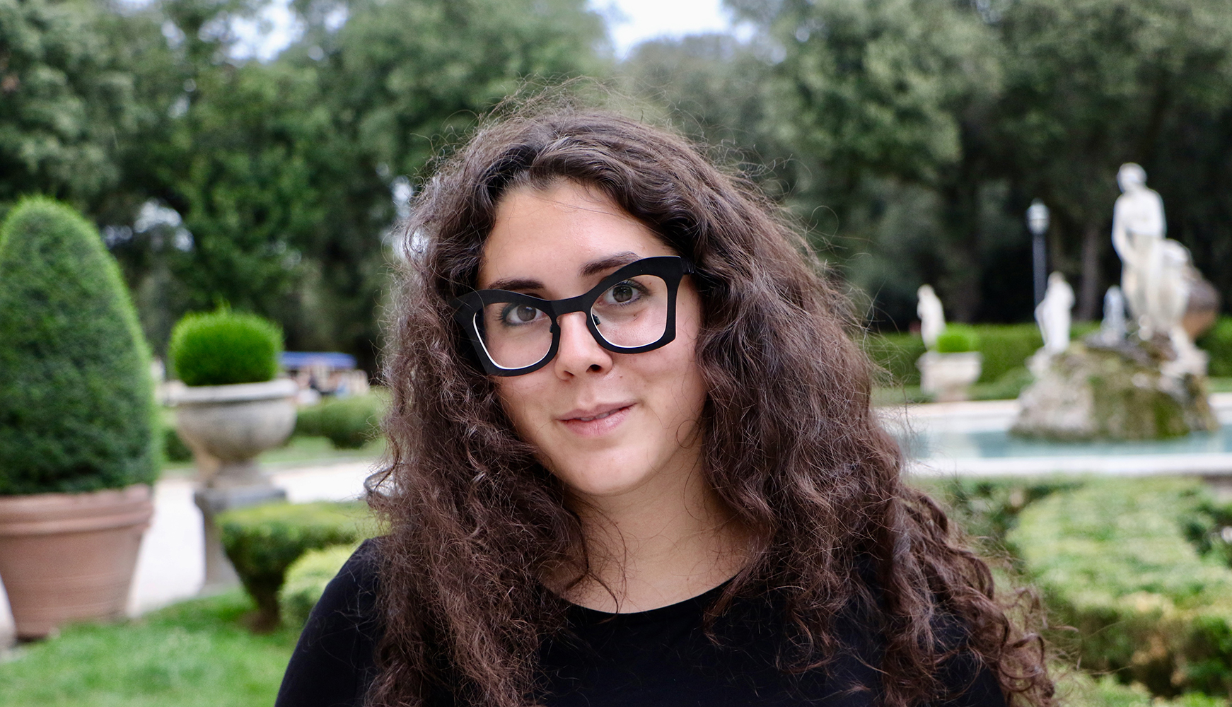Sara L. Petrilli-Jones Color photograph of the head of a light skinned woman with brown hair and wearing glasses; green trees can be seen behind her as she looks at the camera