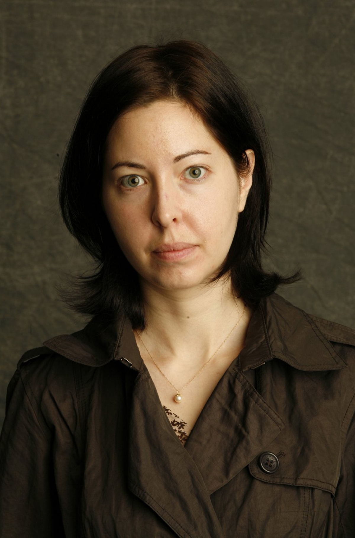 Sarah Manguso Color photograph of the head and torso of a light skinned woman with dark hair looking at the camera with a serious expression