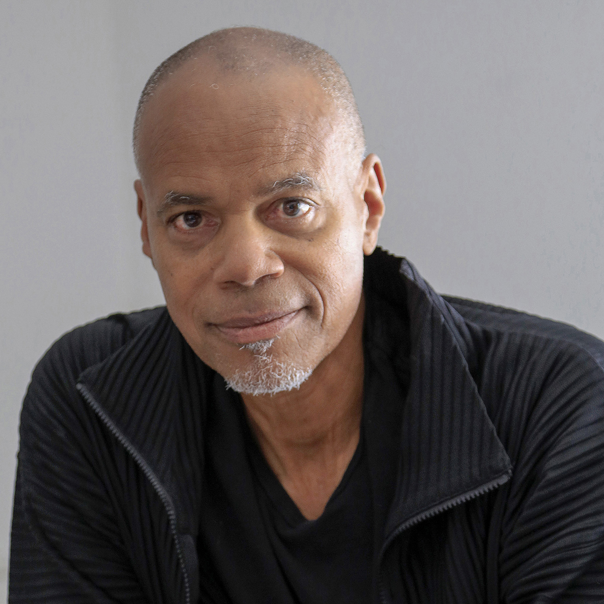 Todd Gray Color photograph of the head and shoulders of a dark skinned man with a slight gray beard and wearing a black jacket with a wide collar, look directly at the camera