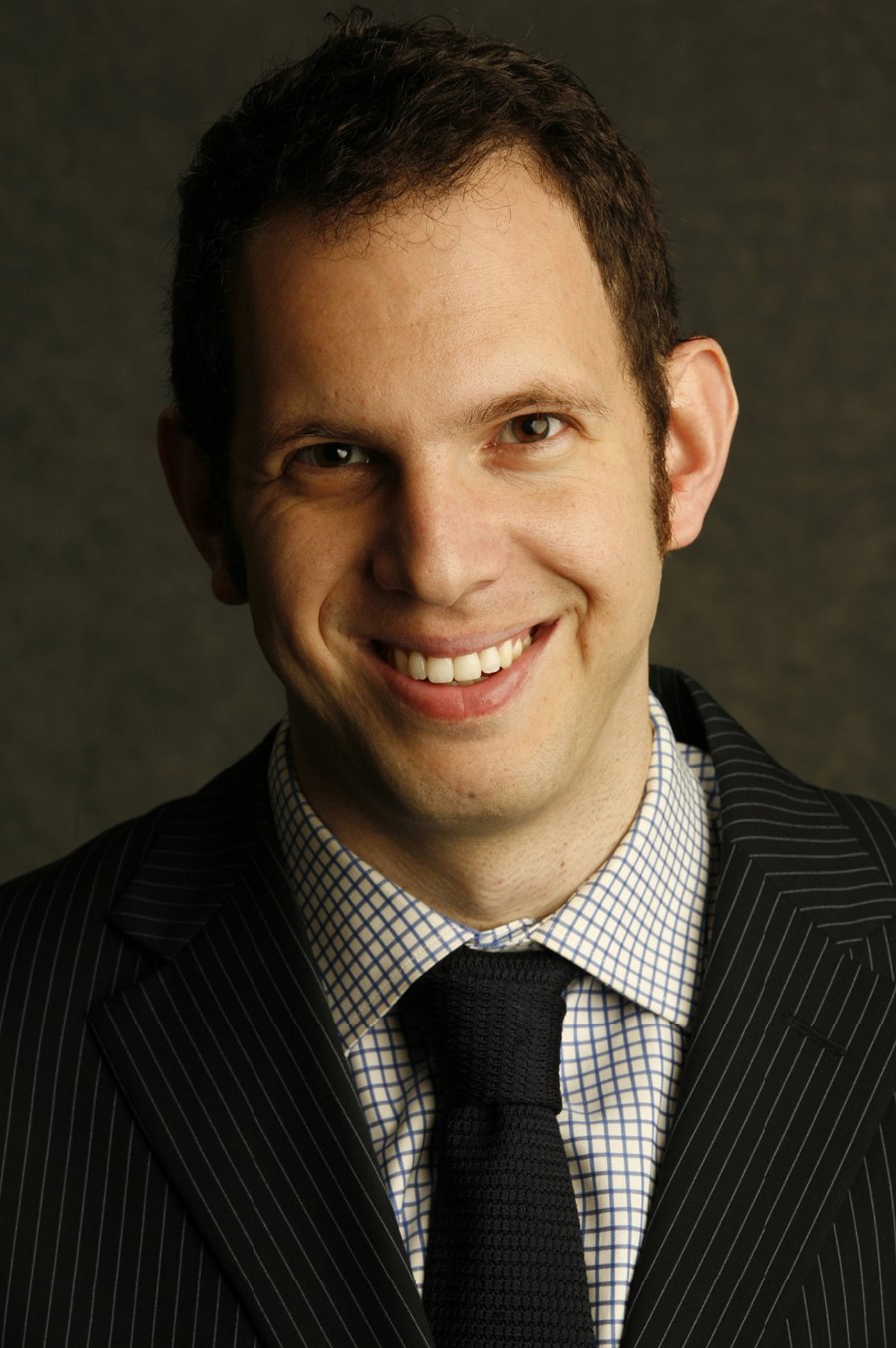 Yotam Haber Color photograph of the head and shoulders of a light skinned man wearing a dark suit and tie and smiling at the camera
