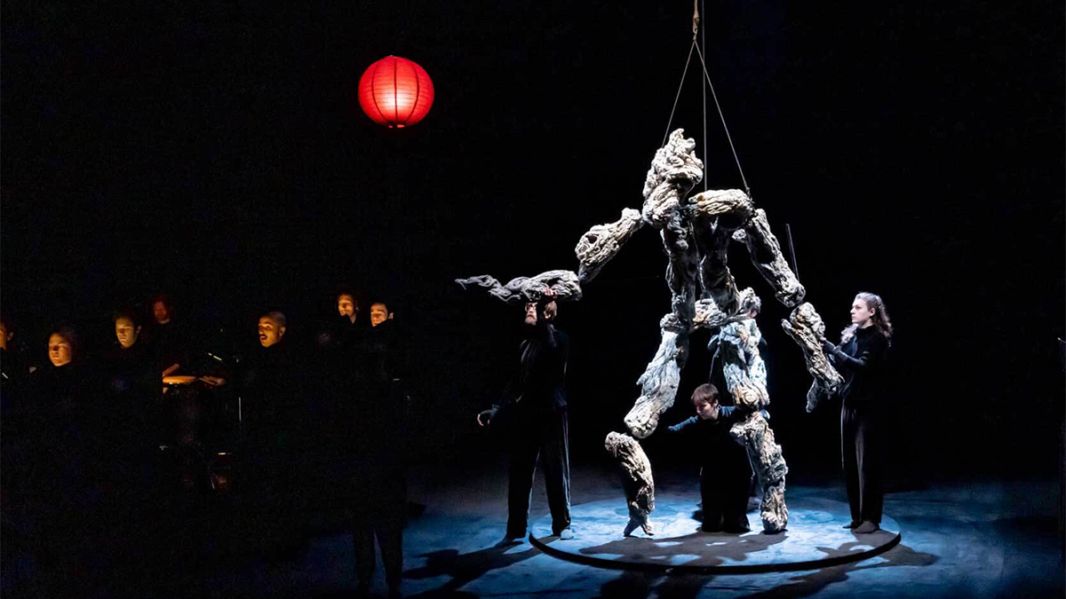 Color photograph of puppeteers dressed in black operated a larger than life sized human shaped puppet