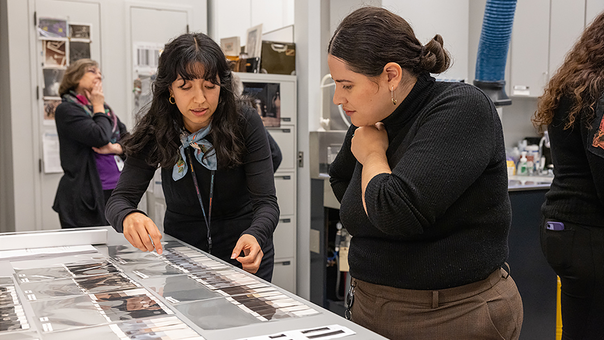 Color photograph of two women looking at works on paper on a table