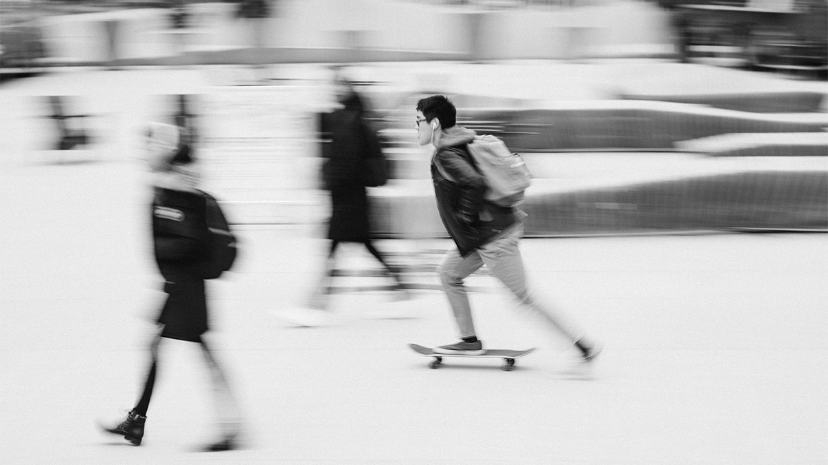 Blurry black and white photo of a public square with a skateboarder and several pedestrians