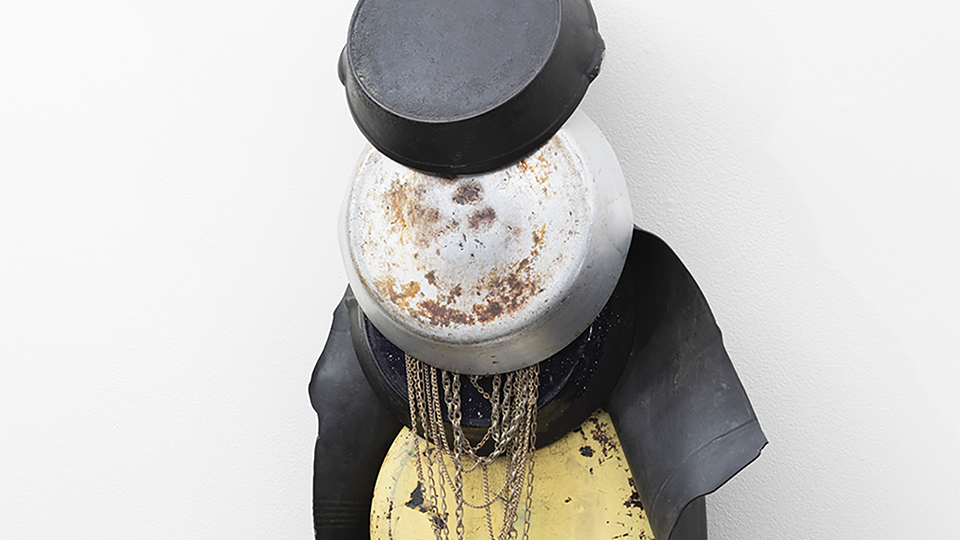 Color photograph of a wall-hanging sculpture made from stove pans, gold necklaces, and more