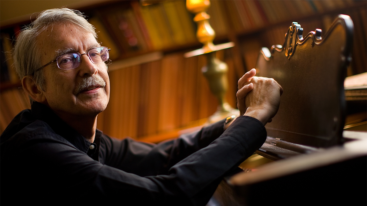 Color photo of an older light skinned man seated at a piano