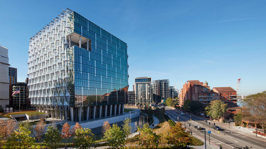 Color photograph of a cubelike twenty-first century glass building surrounded by a moat and standing near a city street