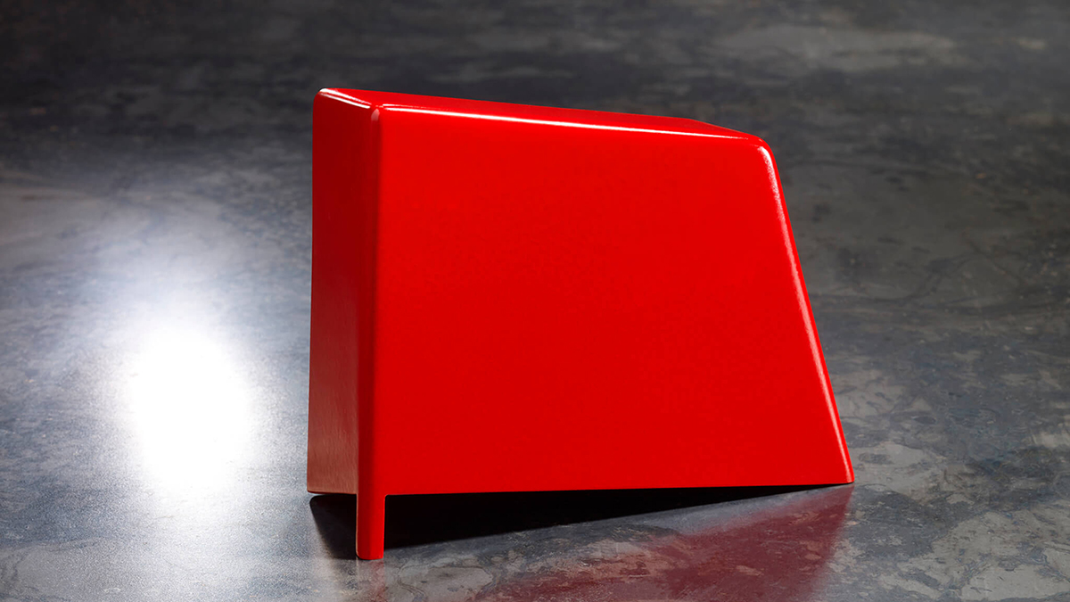 Color photograph of a geometric stool in fire engine red resting a neutral gray stone floor