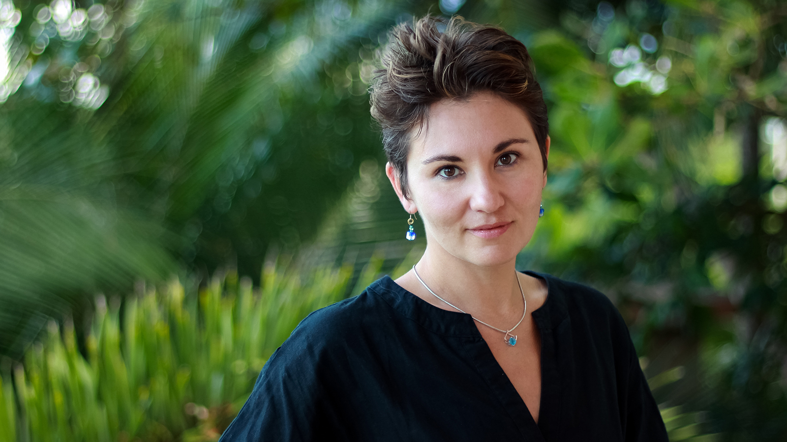 Color photograph of the head and shoulders of Nina C. Young standing outdoors in front of green plants