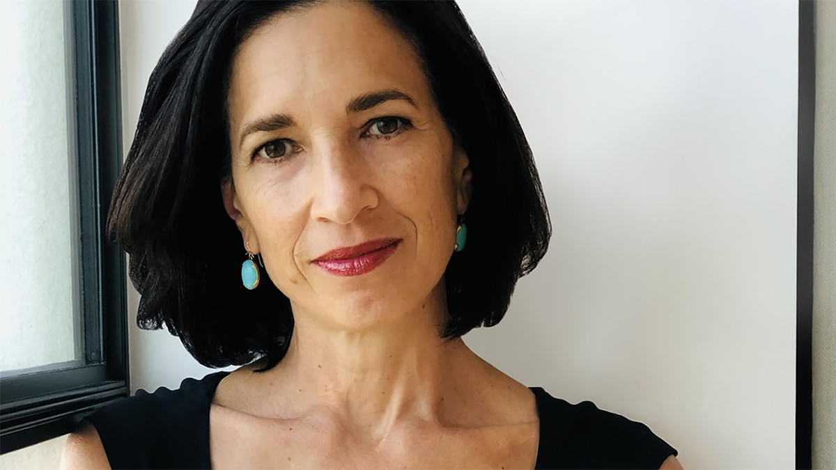 Color photo of the head and shoulders of a light skinned woman with dark hair looking at the camera