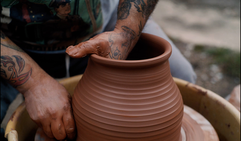 Color photographs of the tattoed brown skinned arms of a man shaping unfired clay on a potter's wheel
