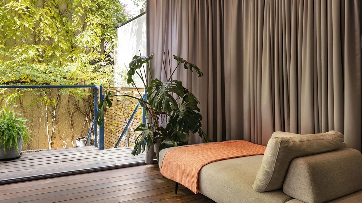 Color photo of a day bed in an apartment room open to a backyard with foliage