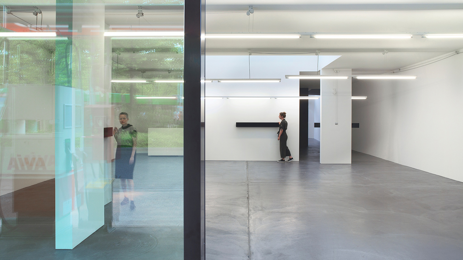 Color photograph of an architectural art installation in a white cube gallery, with two light skinned women visible in the room