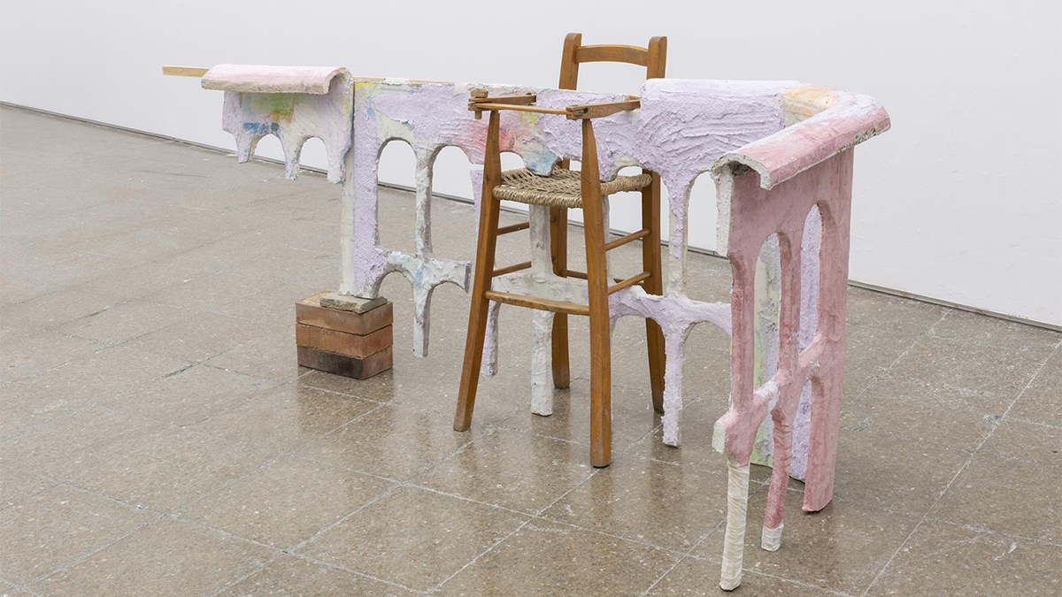 Color photograph of a sculpture, consisting of a wooden baby high chair, red bricks, and pink, purple, and white goo, in a gallery