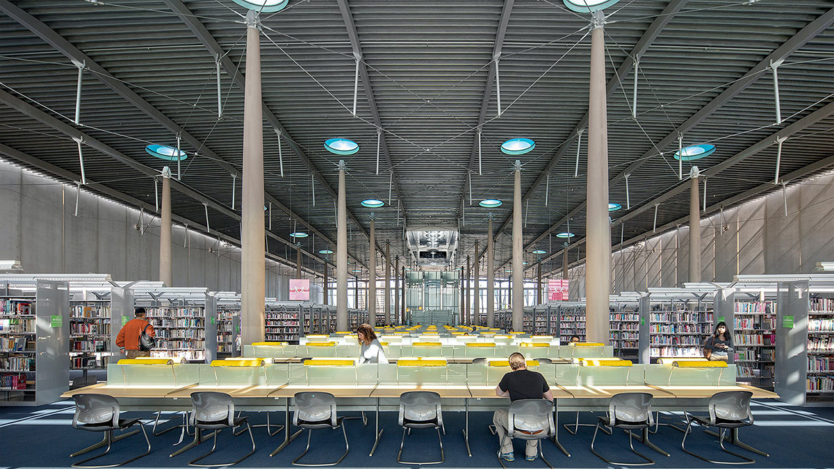 Color photograph of the interior of the Burton Barr Phoenix Central Library, showing long tables flanked by bookshelfs in a large room with pillars