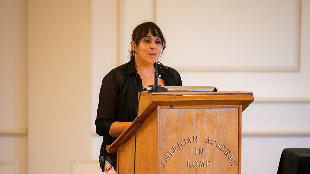 Color photo of a woman standing and speaking at a lecture podium