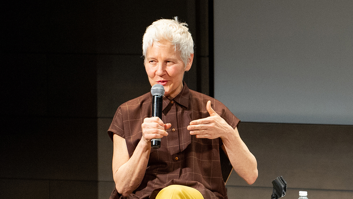 Color photograph of a seated Ann Hamilton holding a microphone and speaking during the 2018 Rome Prize Ceremony
