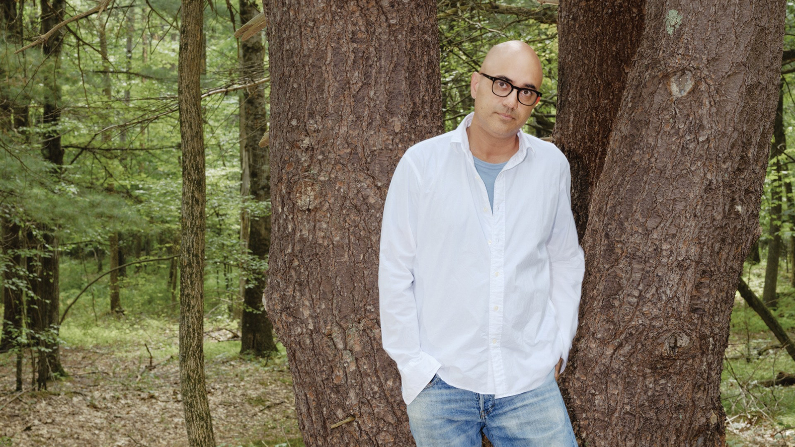Color photograph by Cole Barash of Ayad Akhtar standing in the woods next to a tree